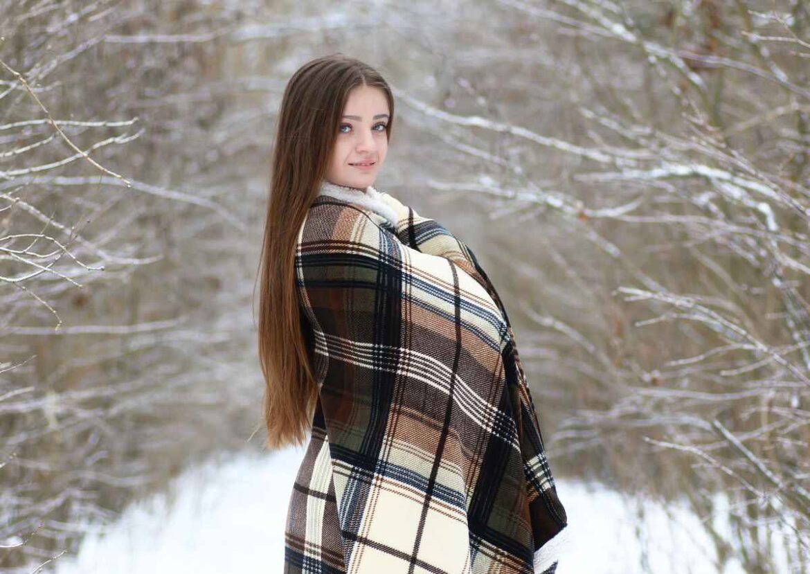 Jeune femme élégante dans un paysage hivernal, enveloppée dans une chaude cape à carreaux, rappelant les capes en maille Devernois.