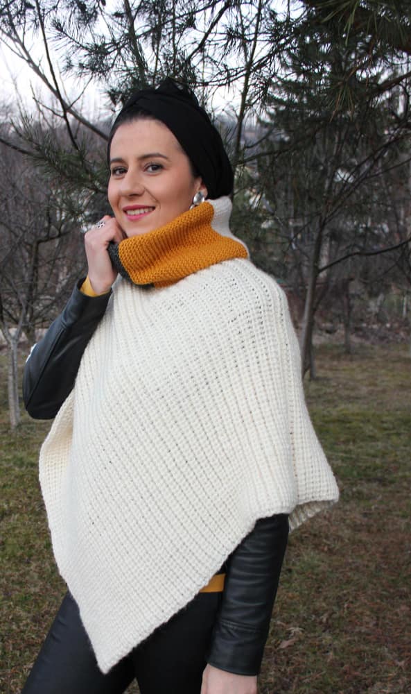 Femme portant un poncho ou une cape en maille blanche épaisse avec un col roulé moutarde, issu de notre collection de capes en maille.